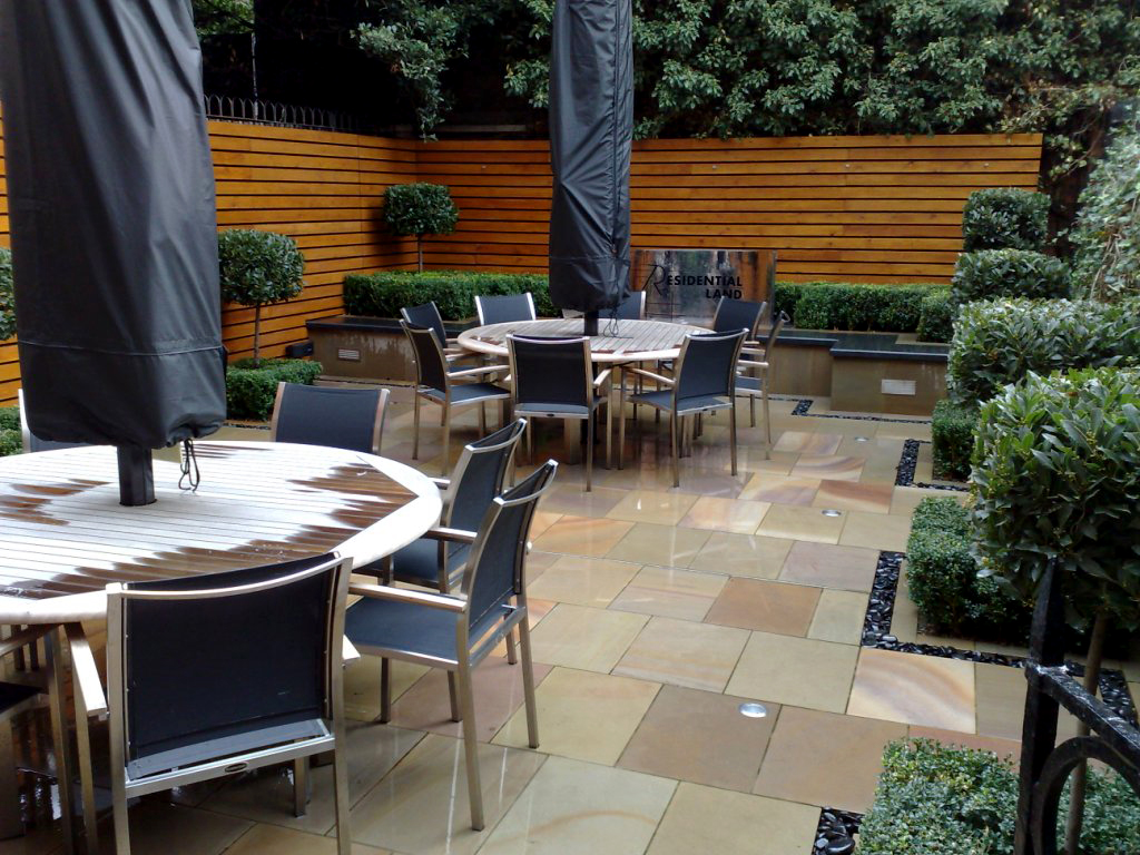 Office staff garden courtyard with table chairs and modern furnishings and clipped bay trees and large umbrella canopies
